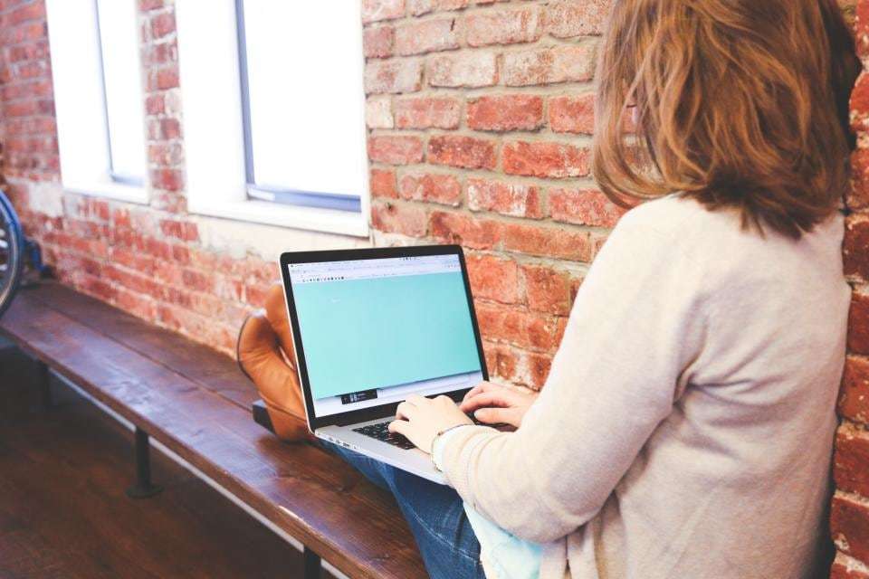 Working on a laptop at a desk by a brick wall