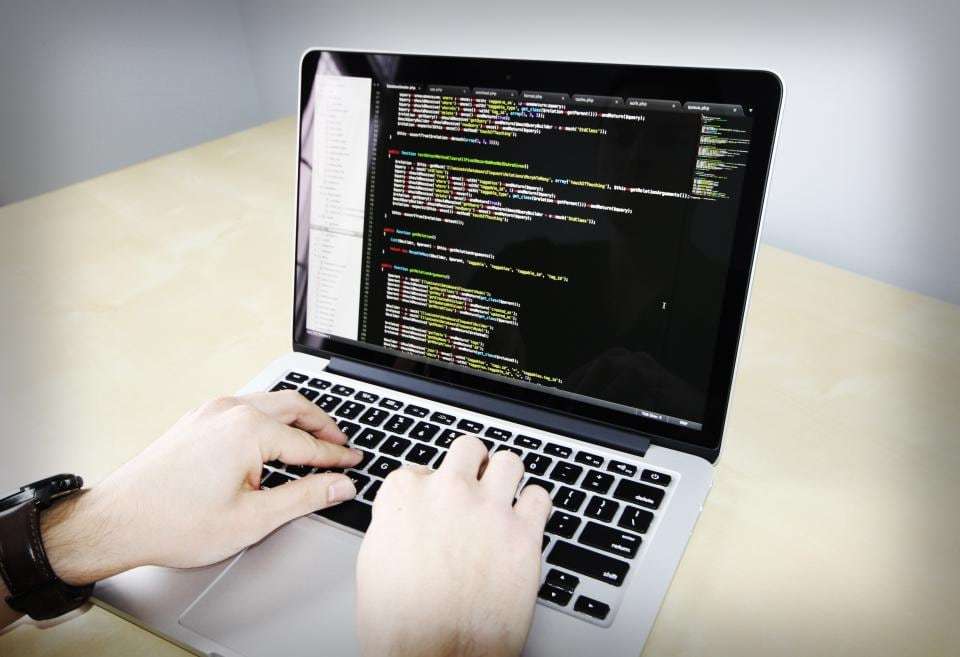 Hands typing website code on a laptop